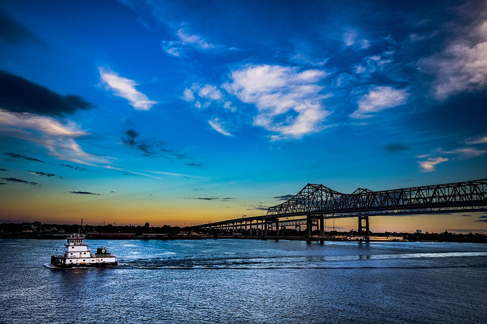 A boat passes beneath a bridge under a vivid blue evening sky